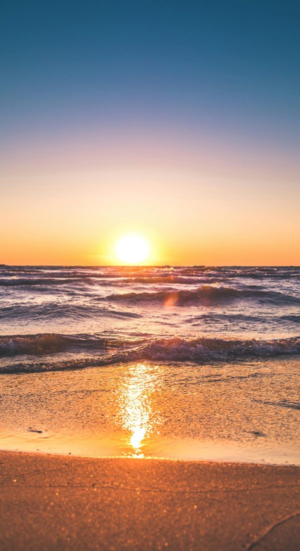 Experience the serene sunset over Ludington Beach with vibrant colors and tranquil waves.